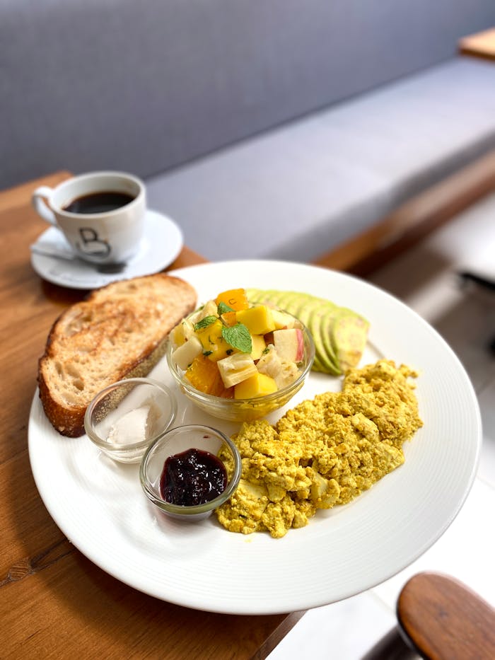 Fresh and colorful vegan breakfast with tofu scramble, fruit bowl, avocado, and coffee.